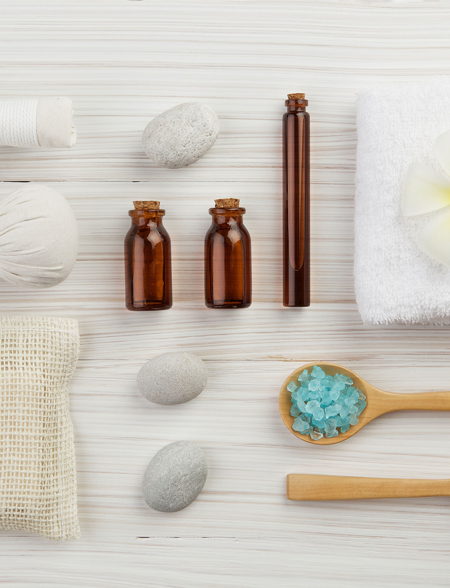 Assorted spa items including amber bottles, sea salt, stones, and towels arranged on a light wooden surface.