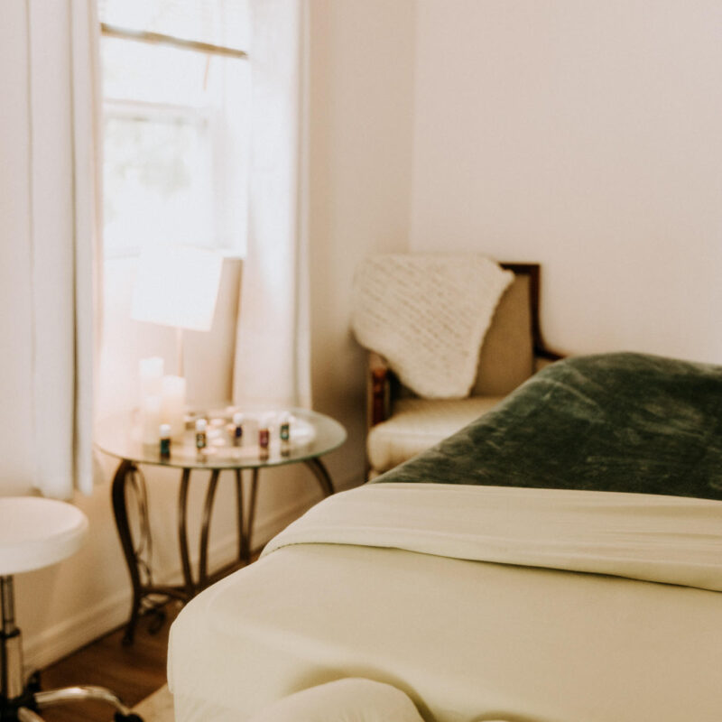 Peaceful massage room with a massage table, cushioned stool, and soft natural lighting.