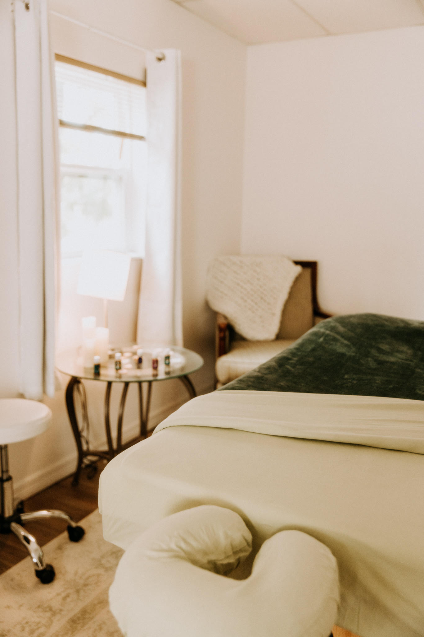 Peaceful massage room with a massage table, cushioned stool, and soft natural lighting.