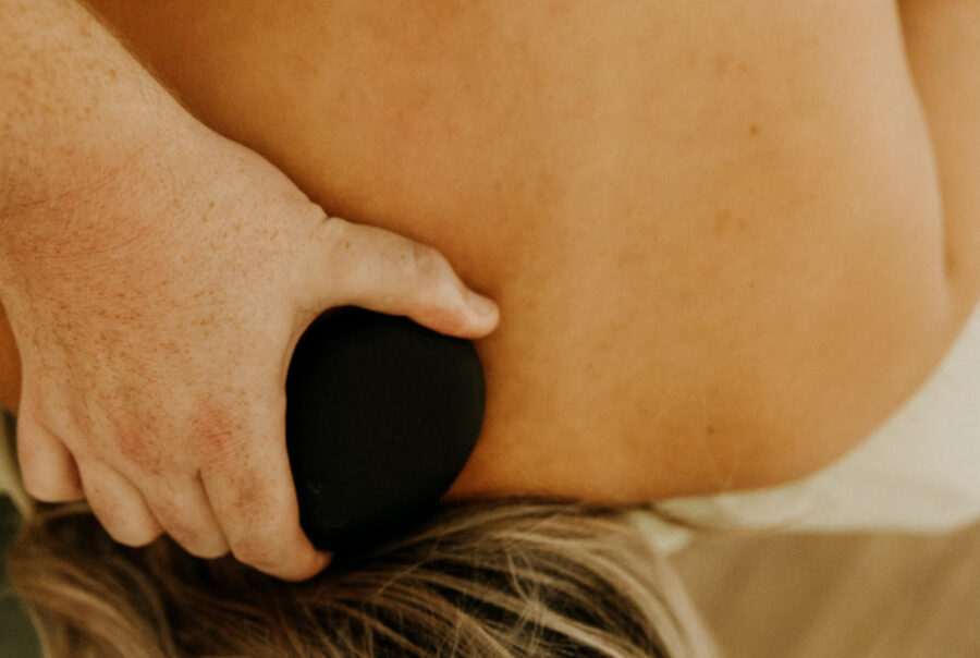 Therapist using a hot stone on a client's back during a massage session, close-up view.