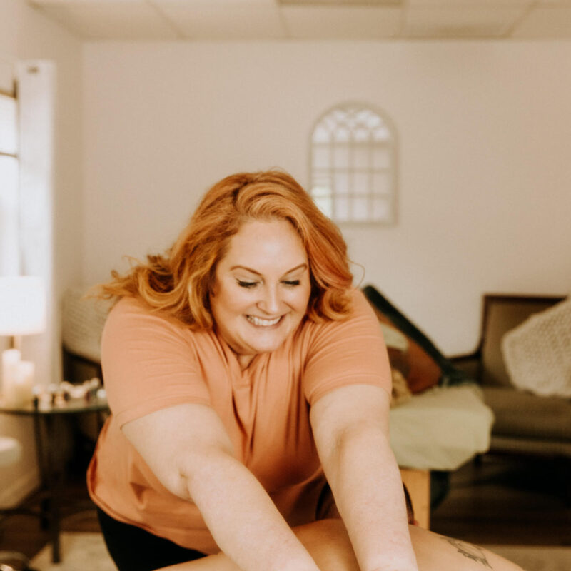 Massage therapist working on a client’s legs, smiling and creating a welcoming atmosphere.