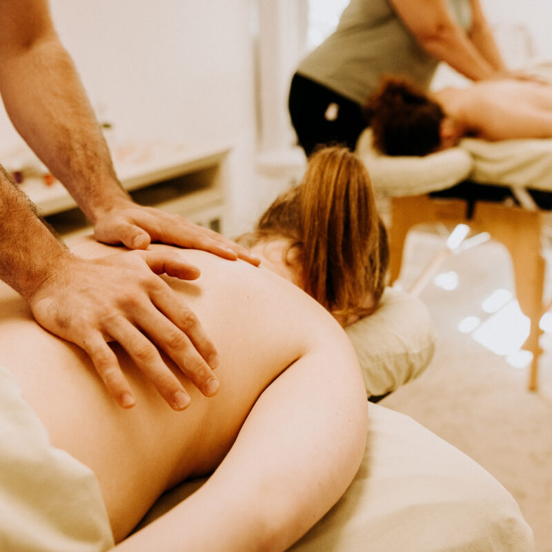 Two people receiving back massages in spa.