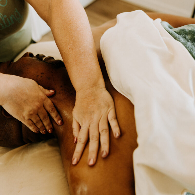 Person receiving shoulder massage, relaxing under blanket.