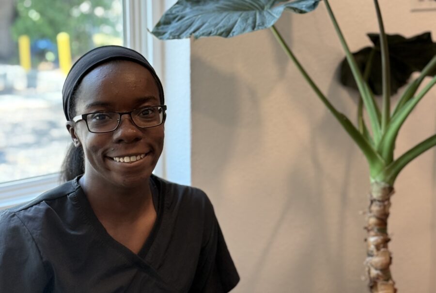 Smiling person in black scrubs beside potted plant.