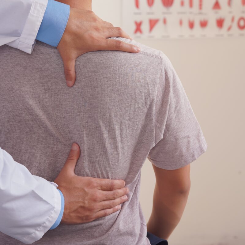 Doctor examining patient's back in clinic.