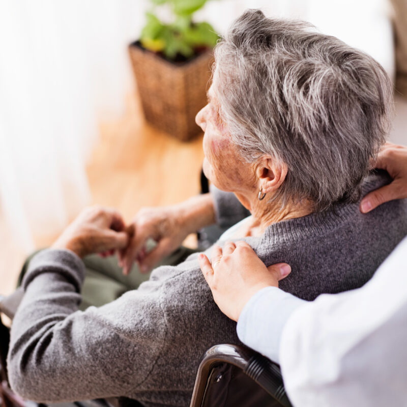 Caregiver comforting elderly person in wheelchair.