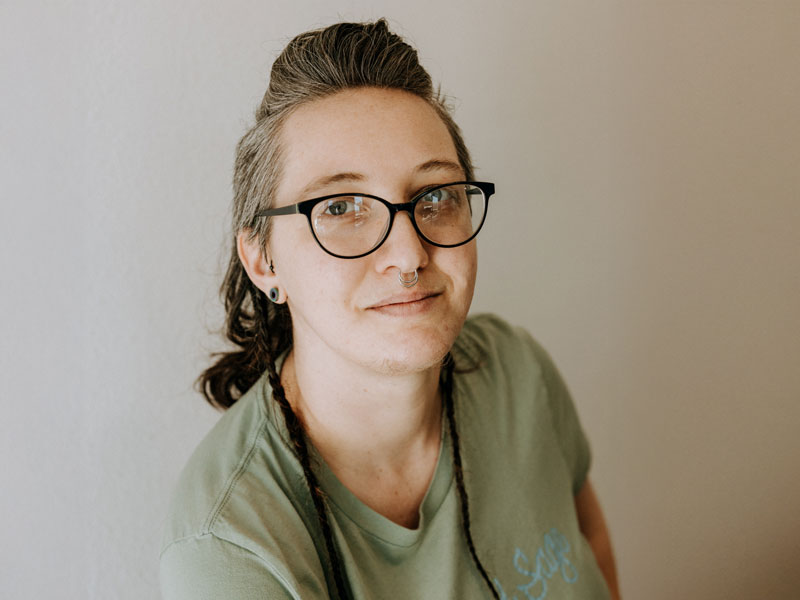 Person with glasses and septum piercing smiling softly.