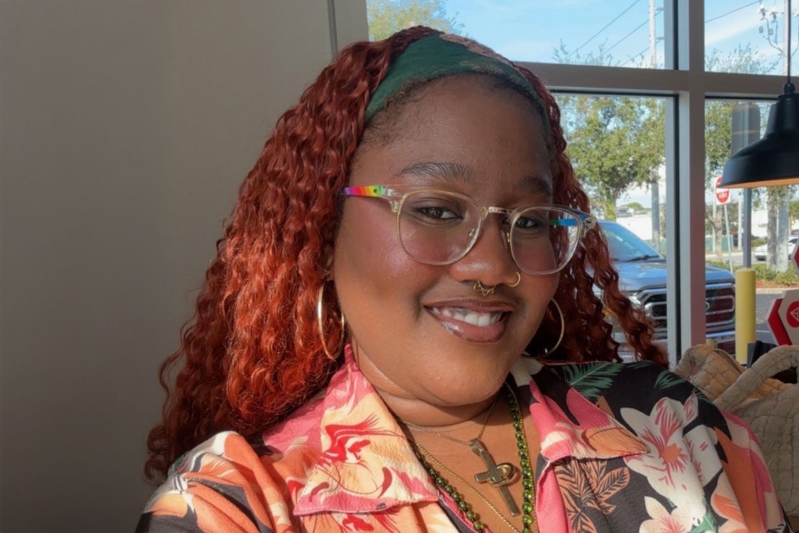 Smiling person with glasses and floral shirt indoors.