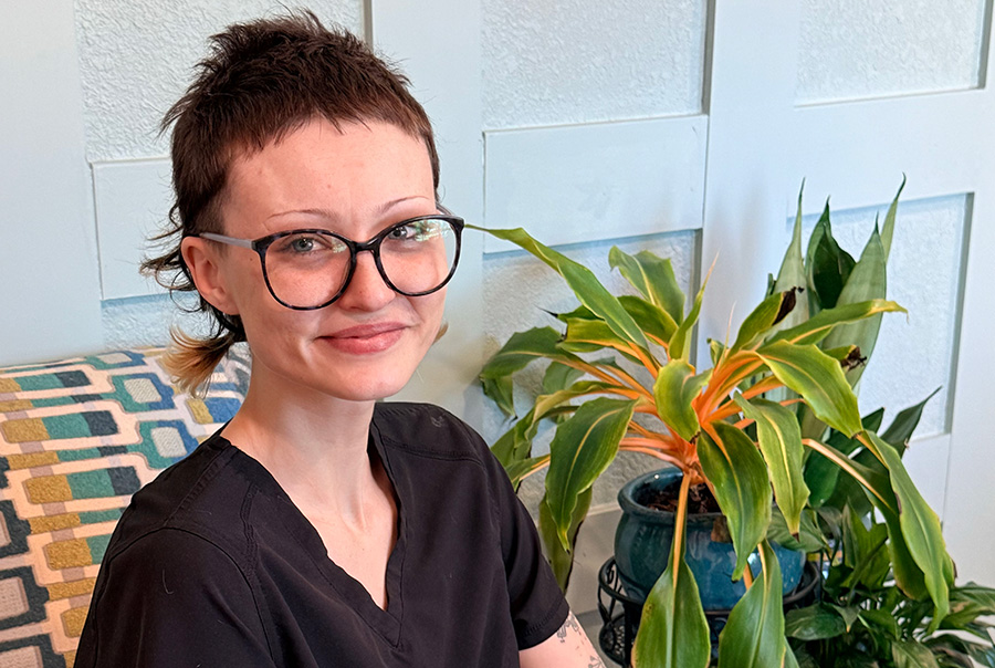 Smiling person with glasses and plants indoors.