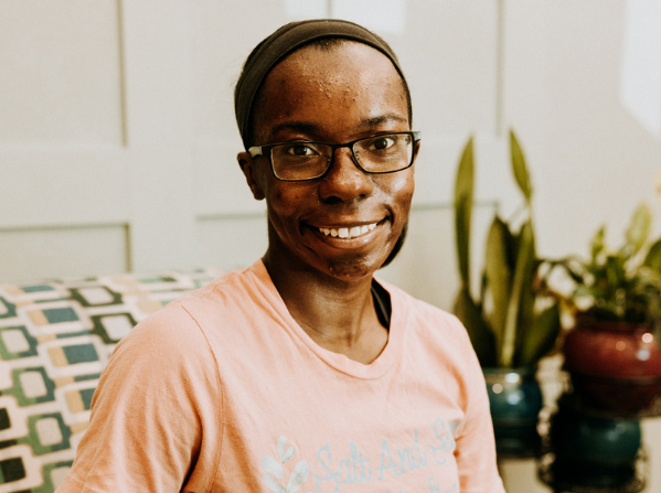 Smiling person wearing glasses, sitting indoors near plants.