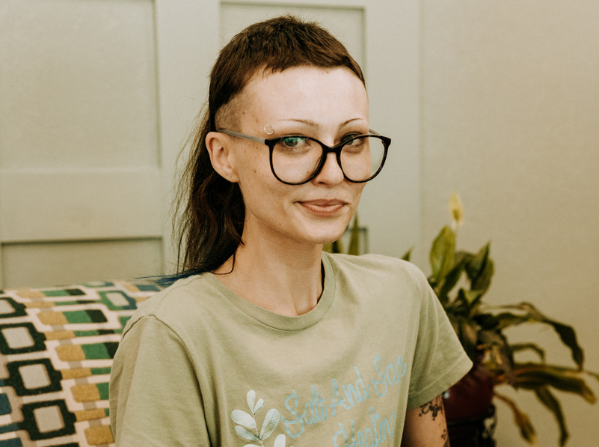 Person with glasses smiling indoors, plant in background.
