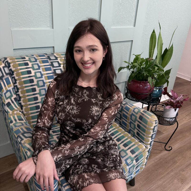 Woman sitting on patterned chair, smiling indoors.